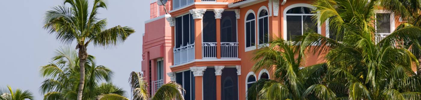 Orange roofed building with four floors surrounded by palm trees.